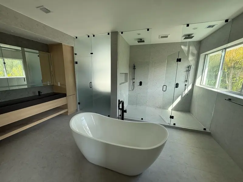 Freestanding tub in front of a glass walk-in shower with black hardware