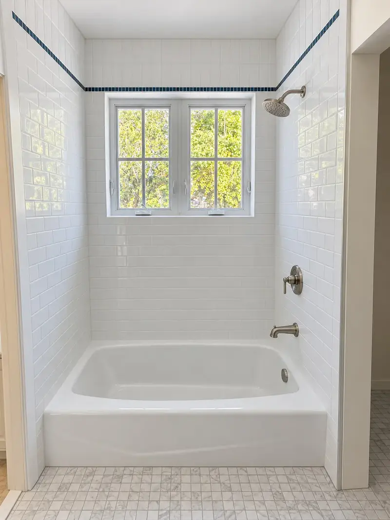 White subway-tile tub and shower with a navy accent band and window
